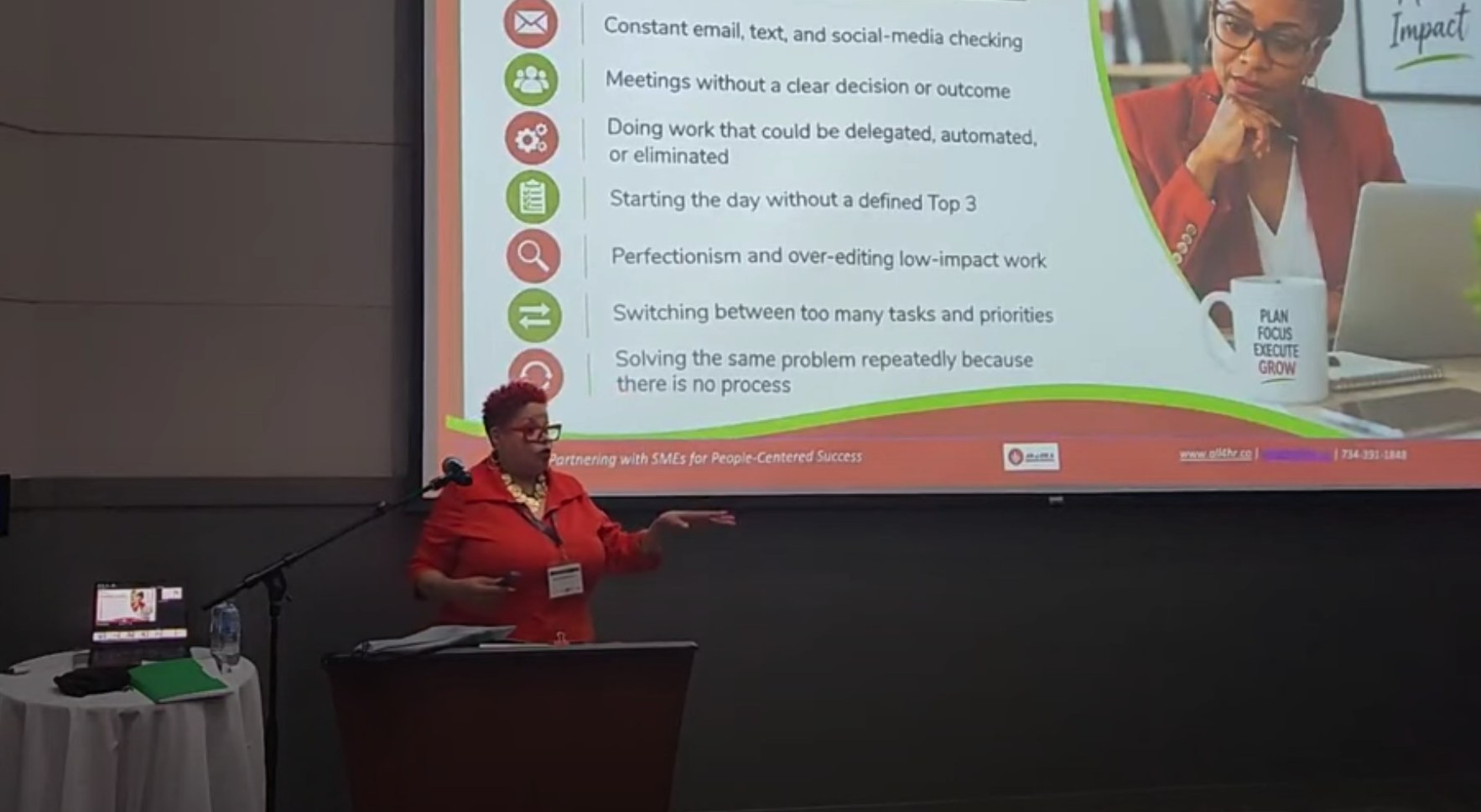 April D. Halliburton presenting From Busy to Strategic to a live audience, gesturing toward a slide of everyday time drains